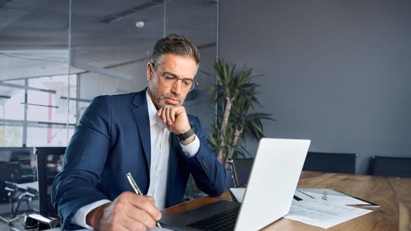 Middle Aged Professional In A Blue Suite Focusing As He Works On The Computer
