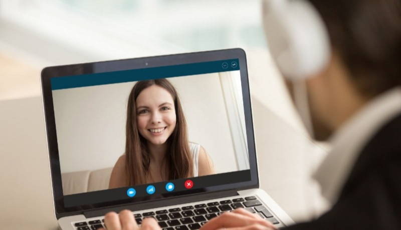 Man with headphones and laptop speaking to women over video chat